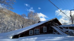 A wooden cabin with a steep roof, a staircase leading to the entrance, and a snow-covered landscape. - Takara Onsen Pension Satchimo (Kitashiobara)