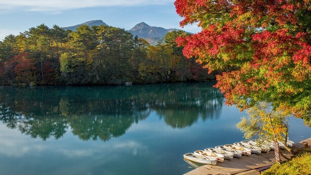 A calm lake with boats docked on a wooden pier, surrounded by autumn-colored trees and mountains in the background. - Takara Onsen Pension Satchimo (Kitashiobara)
