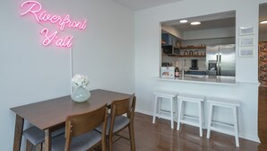 A modern kitchen with a neon sign, wooden dining table, and white bar stools. - ❤️ of DWNTWN, Riverfront w pool, walk 2 Broadway (Nashville)