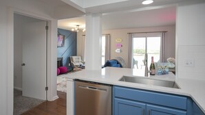 A modern kitchen with a dishwasher, blue cabinets, and a dining area with a chair and table. - ❤️ of DWNTWN, Riverfront w pool, walk 2 Broadway (Nashville)