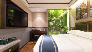 Une chambre d’hôtel équipée d’un lit, d’un bureau, d’une télévision et d’une grande fenêtre donnant sur un paysage verdoyant.