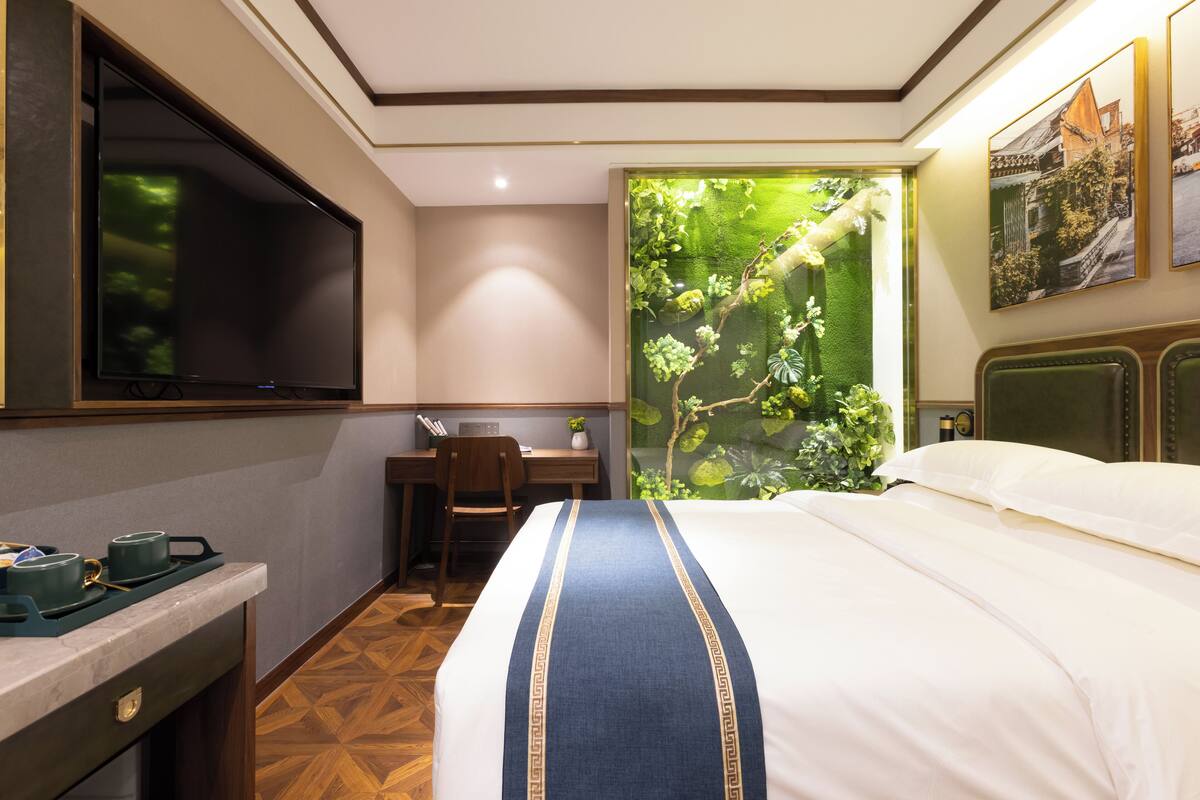 Une chambre d’hôtel équipée d’un lit, d’un bureau, d’une télévision et d’une grande fenêtre donnant sur un paysage verdoyant.