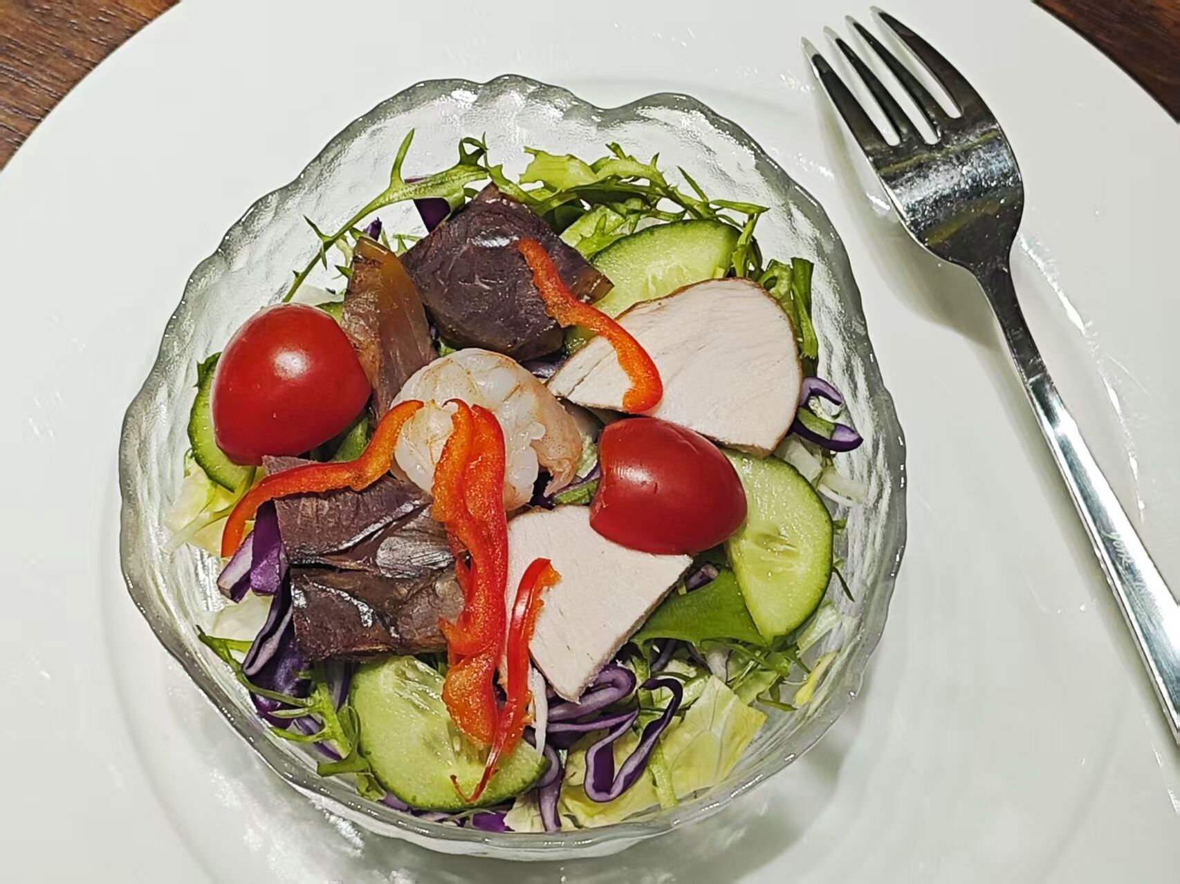 Une salade composée de divers légumes et de viande, servie dans une assiette blanche.