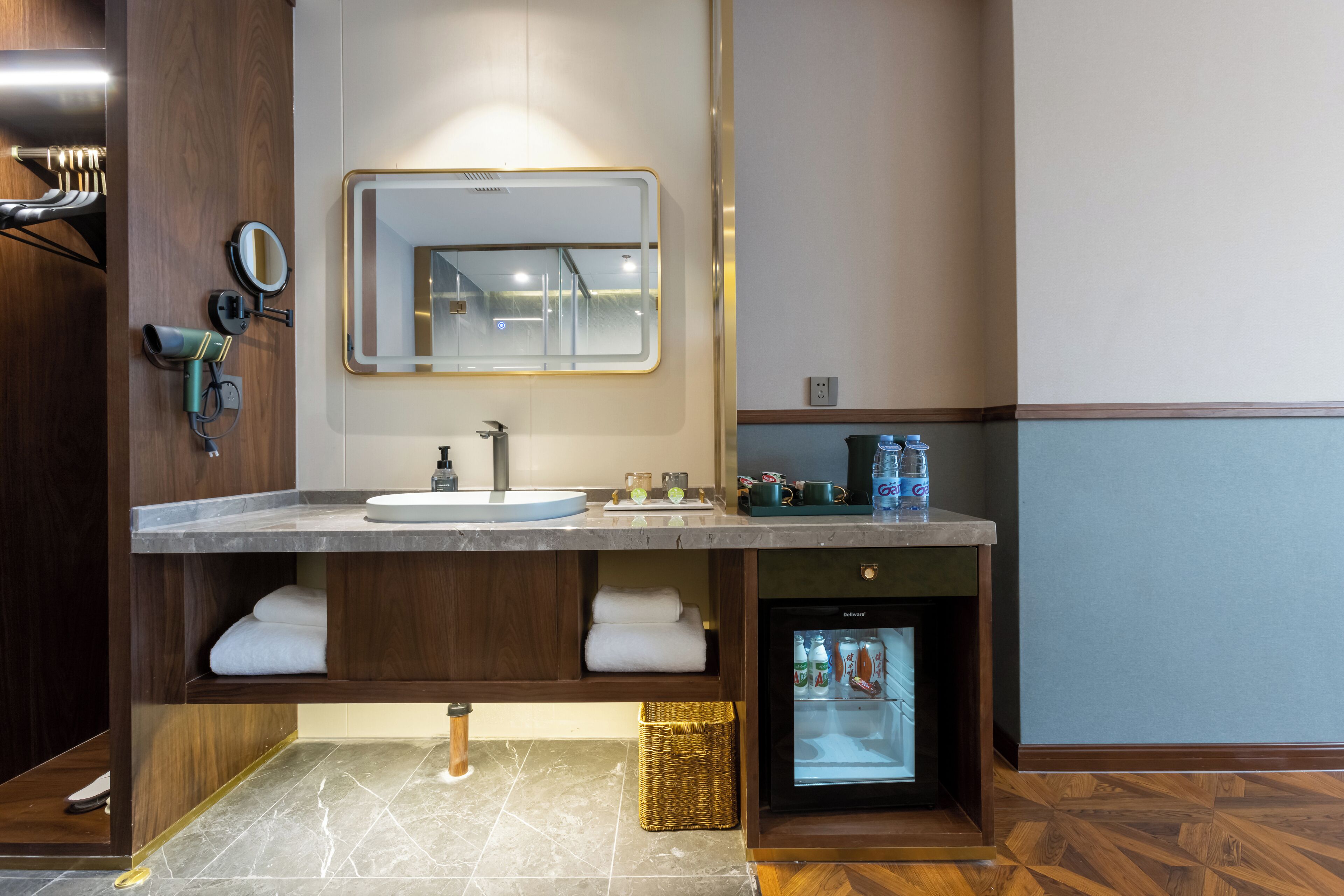 A modern bathroom with a built-in sink, a mirror, a hairdryer, a mini fridge, and a towel rack.