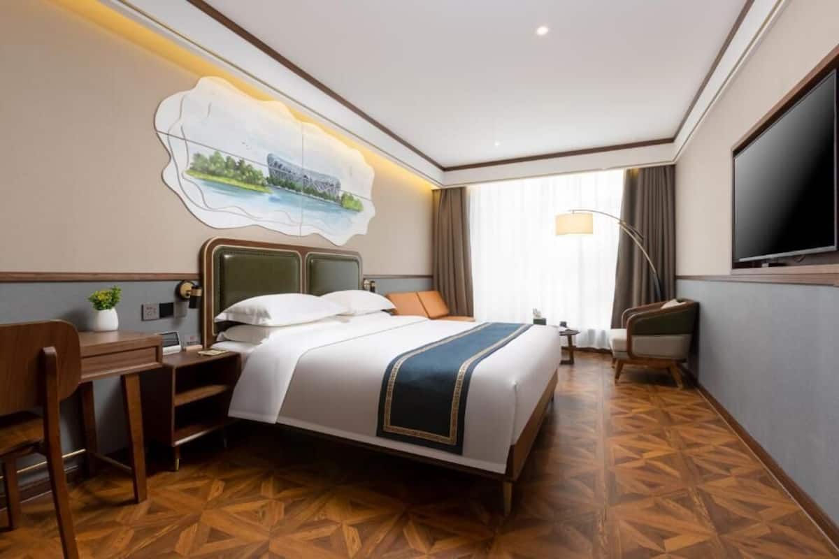 Une chambre d’hôtel avec un grand lit, un bureau, une chaise, une télévision et un tableau au mur.
