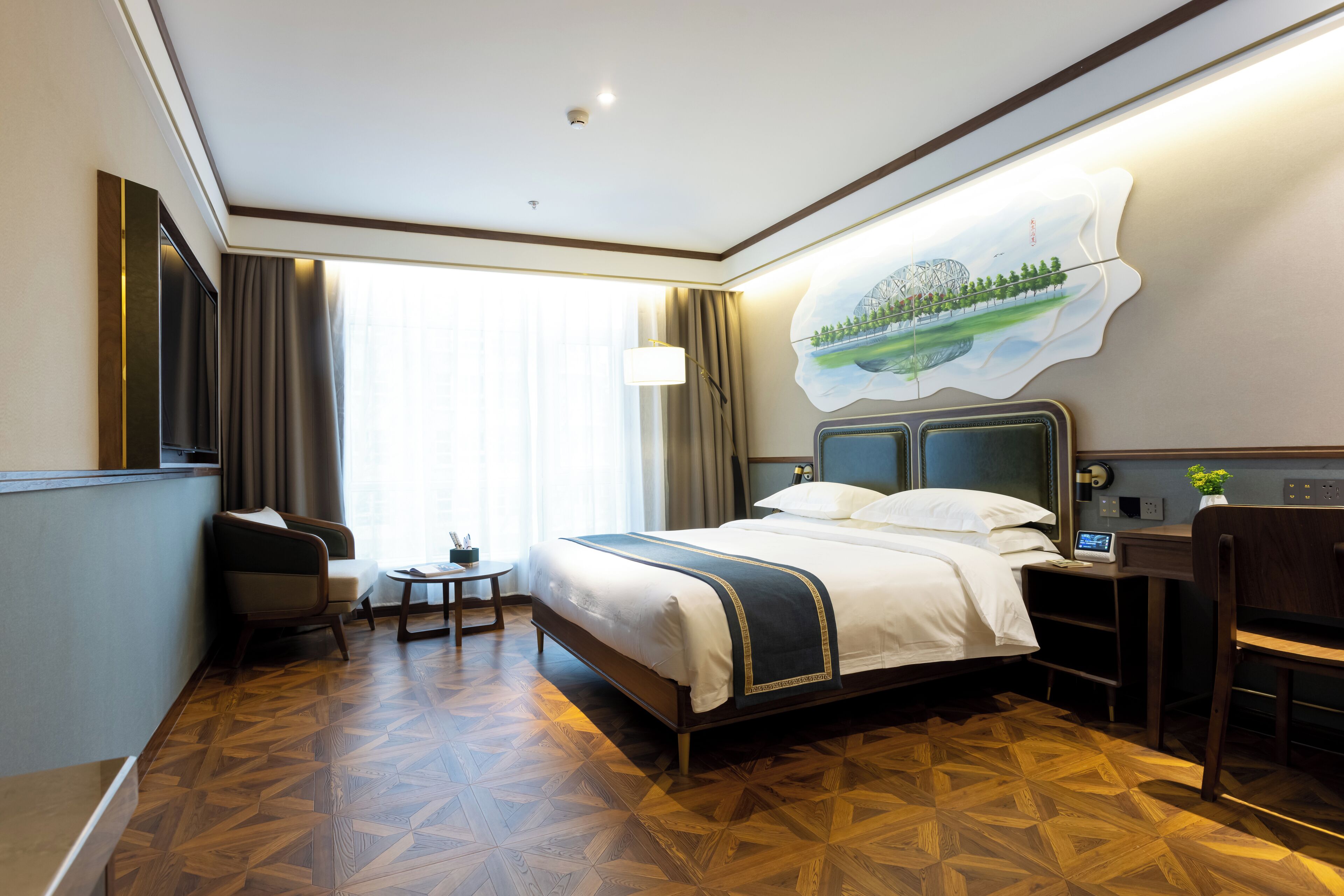 A hotel room with a large bed, a desk, a chair, a small table, and a painting on the wall.
