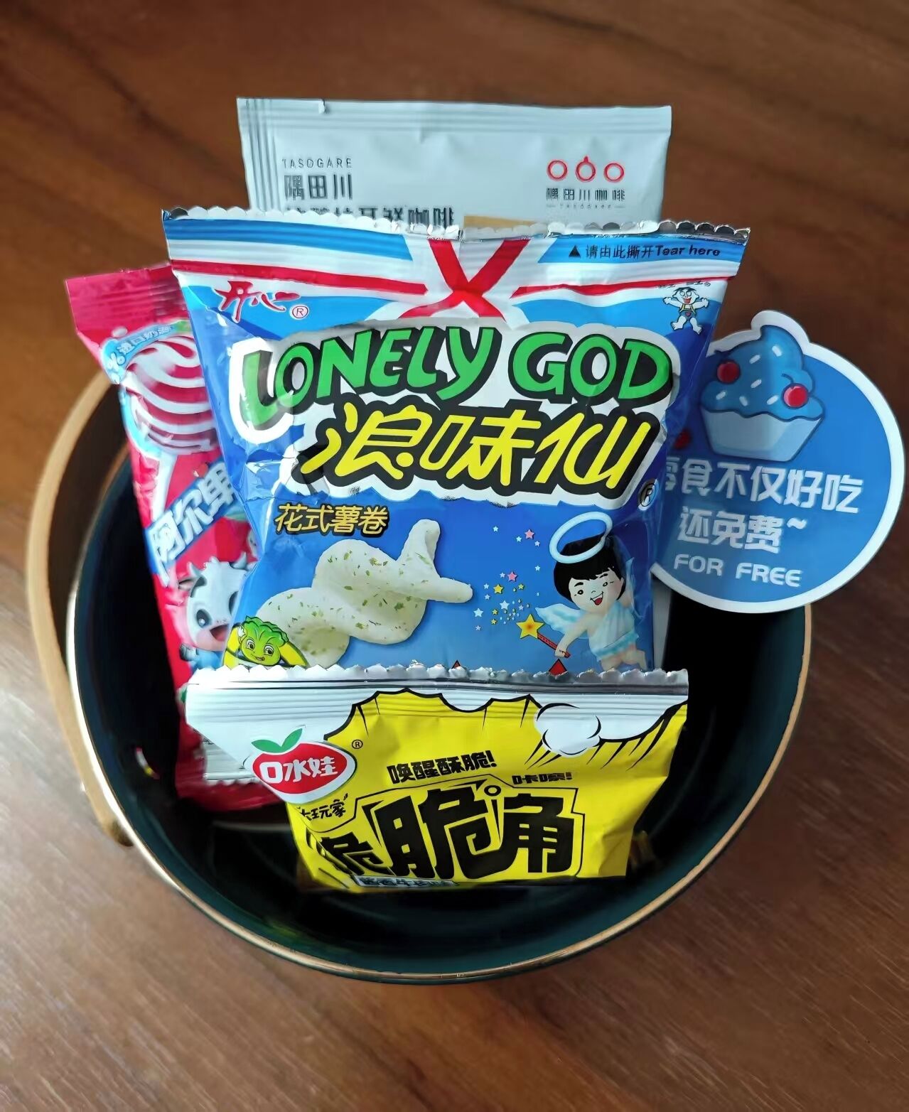 Een schaal met diverse snacks, waaronder een zakje 'Lonely God' snacks, een snack in rood-witte verpakking, en een gele snackverpakking.