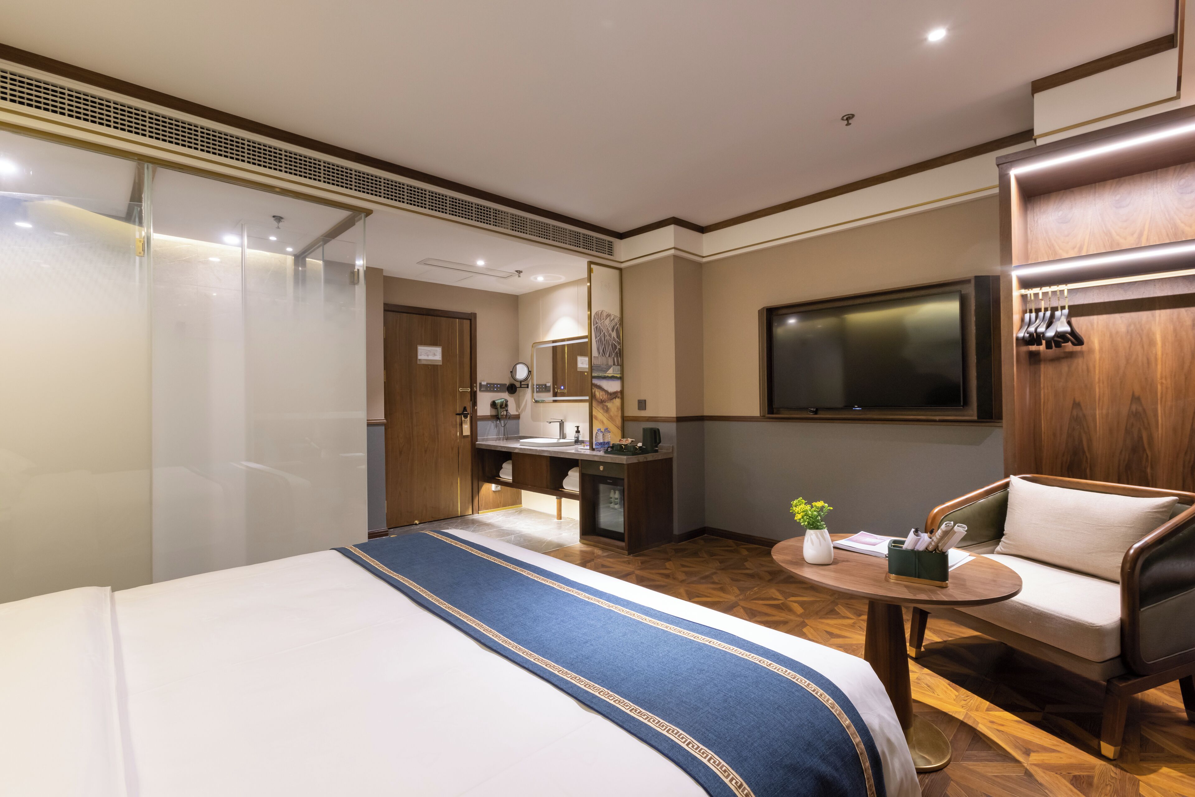 A hotel room with a large bed, a desk with a mirror, a television, and a seating area with a table and chairs.