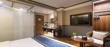 A hotel room with a large bed, a desk with a mirror, a television, and a seating area with a table and chairs.