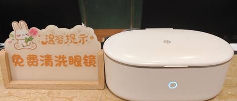 A white portable device with a blue light indicator, placed on a marble floor next to a wooden stand with a sign featuring a cartoon rabbit and Chinese text.