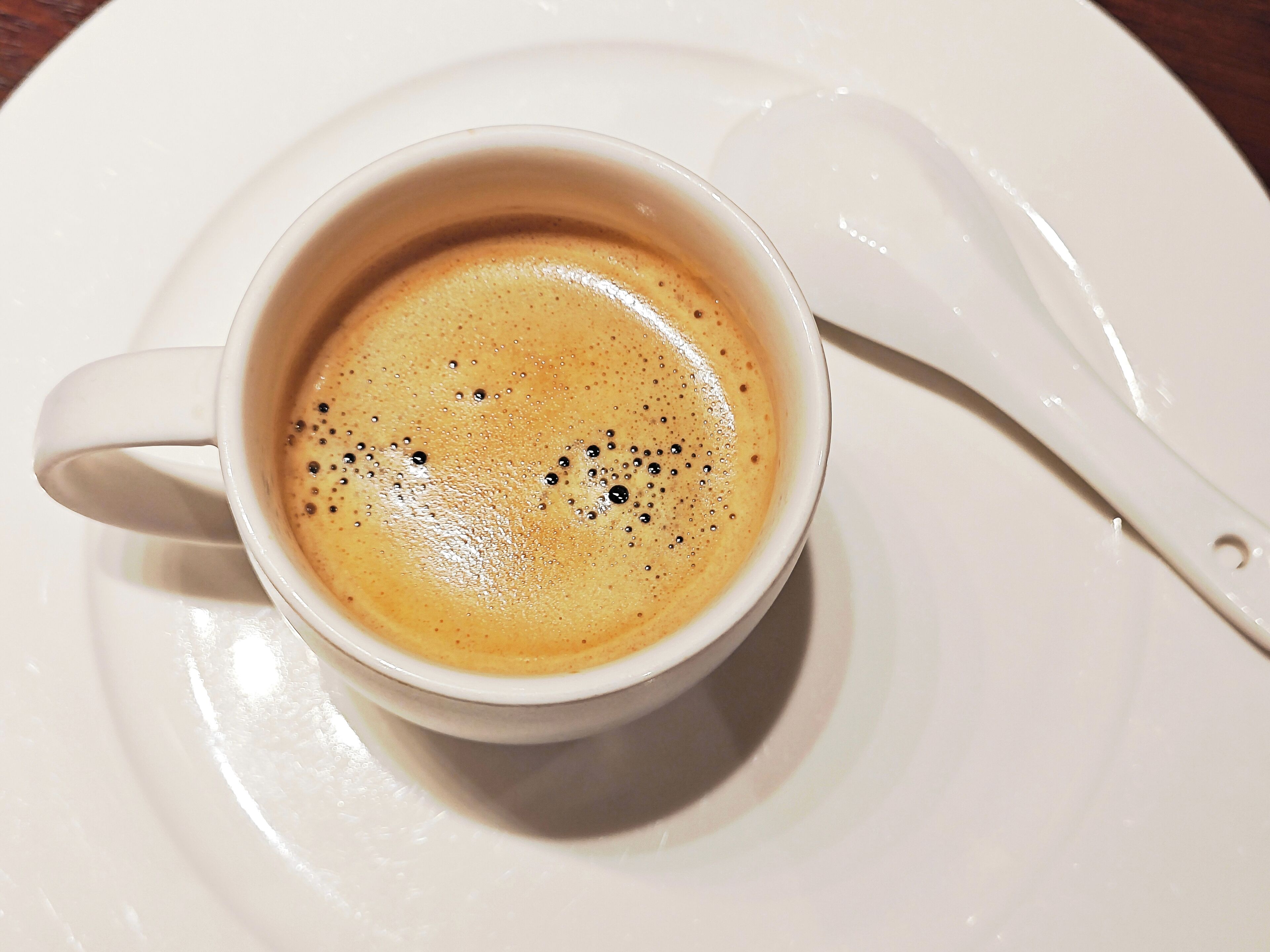 A white cup of coffee with a spoon on a white plate.