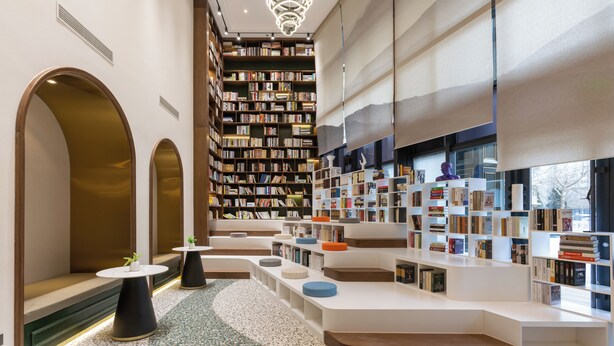 Eine moderne Bibliothek mit Bücherregalen, Sitzbereichen und einer außergewöhnlichen Deckenleuchte.