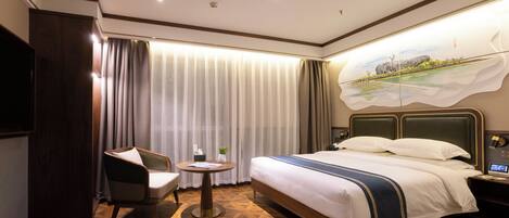 A hotel room with a large bed, a chair, a small table, and a painting on the wall.