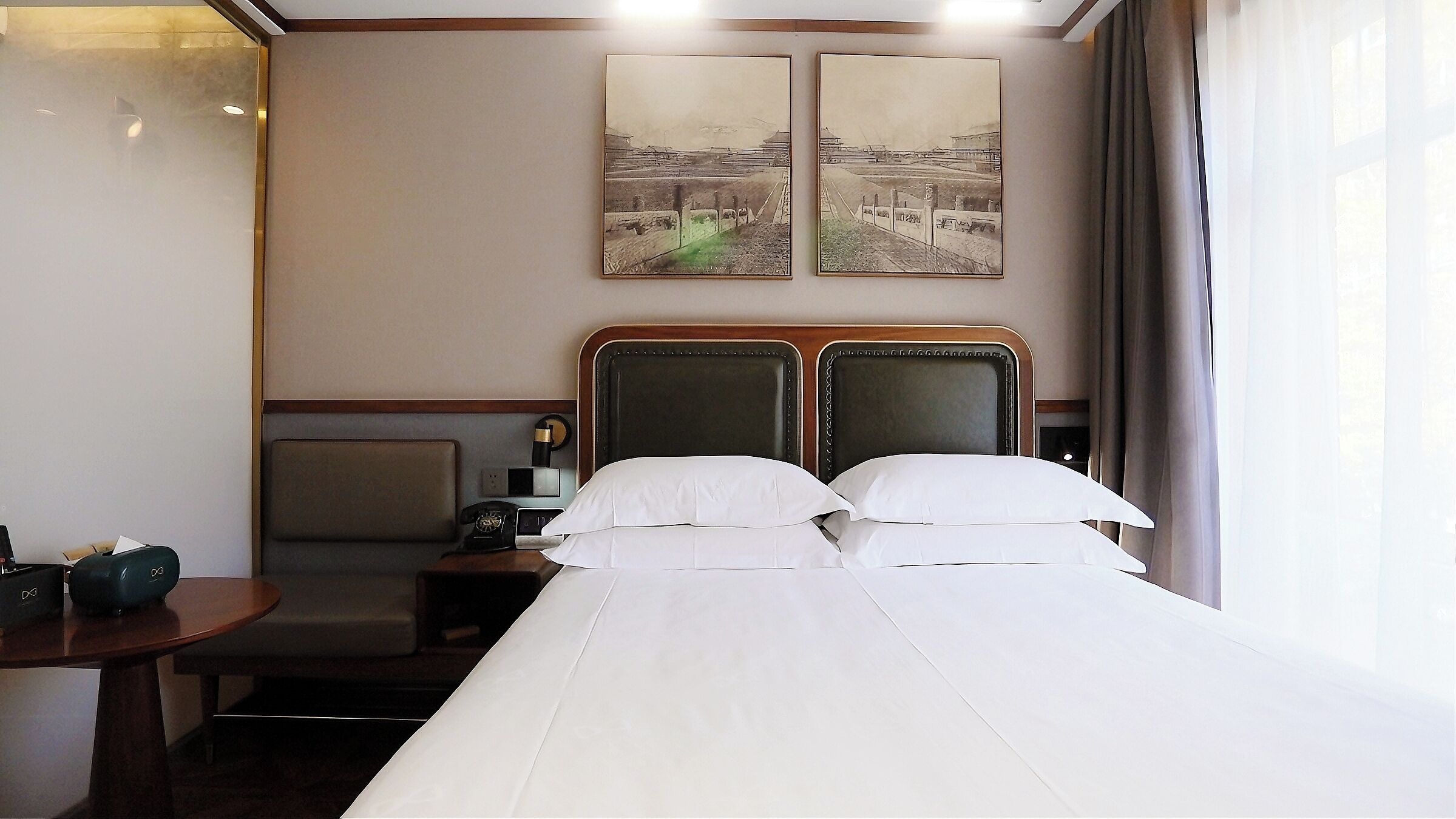 A hotel room with a bed, a desk, and two paintings on the wall.
