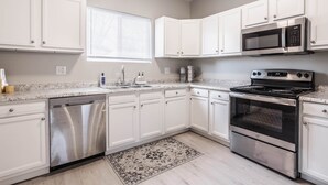 A modern kitchen with white cabinets, stainless steel appliances, a dishwasher, and a microwave. - Grand Park, Westfield, Space For Entire Team, Sleeps 30 comfortably. Unit A (Sheridan)
