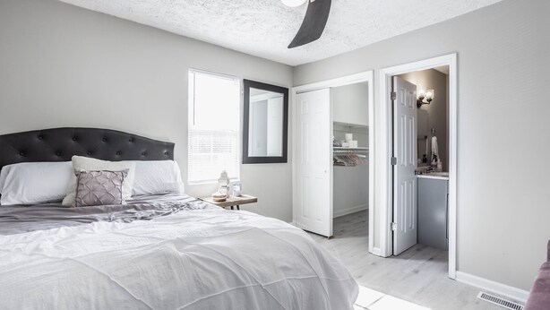 A bedroom with a large bed, a nightstand, a mirror, and a walk-in closet. - Grand Park, Westfield, Space For Entire Team, Sleeps 30 comfortably. Unit A (Sheridan)
