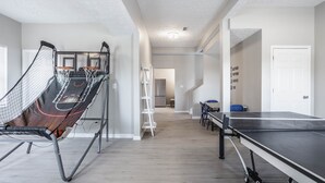 A spacious room with a ping pong table, a basketball hoop, and a ladder. - Grand Park, Westfield, Space For Entire Team, Sleeps 30 comfortably. Unit A (Sheridan)
