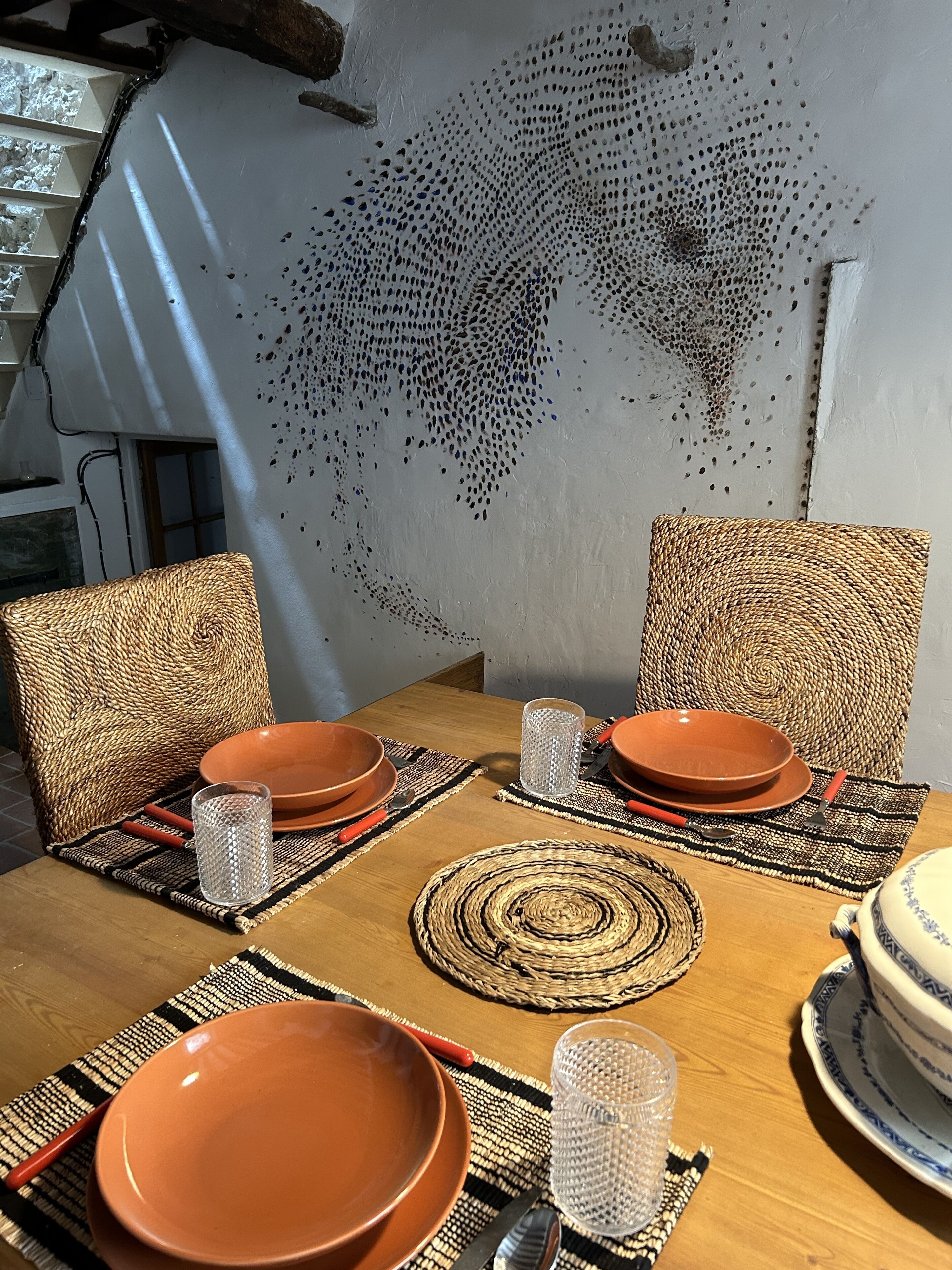 Una mesa de comedor dispuesta con platos marrones, vasos transparentes y protectores de mesa tejidos.