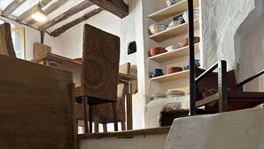 A rustic interior with stone steps leading to a wooden door, a woven chair, and shelves with dishes. - La Bergerie (MIRABEL AUX BARONNIES)