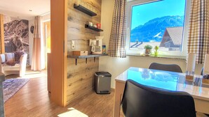 Eine moderne Küche mit Holzelementen, ein Essbereich mit einem Glastisch und Blick auf Berge durch ein Fenster.
