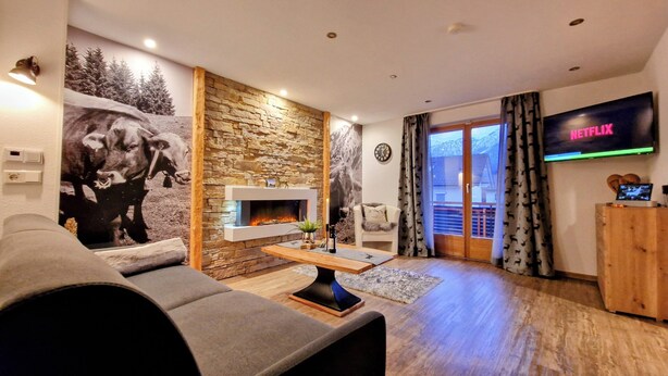 Ein Wohnzimmer mit Steinwand, Kamin, einer Couch, einem Fernseher und Blick durch eine Glastür.