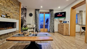 Ein modernes Wohnzimmer mit Kamin, Esstisch und einem Fernseher, der 'NETFLIX' anzeigt.