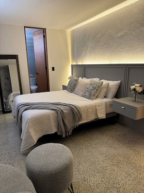 A modern bedroom with a bed, bedside table, and a nightstand with a vase of flowers.