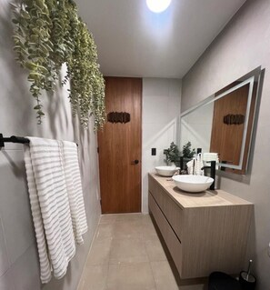 A modern bathroom with a wooden door, a large mirror, and a white sink.