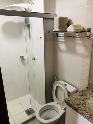 A bathroom with a glass-enclosed shower, a toilet, and a shelf with toiletries. - Veredas do Rio Quente (Rio Quente)