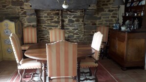Un comedor con pared de piedra, una mesa redonda de madera, sillas tapizadas a rayas y una lámpara colgante.