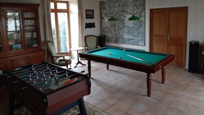 Una habitación con mesa de billar, mesa de futbolín y un amplio ventanal con cortinas.