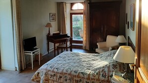 Habitación de hotel con cama, escritorio, silla, televisor y ventana con cortinas.