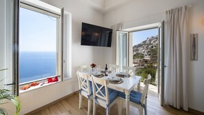 Un coin repas avec une table dressée pour quatre personnes, de grandes fenêtres offrant une vue sur la mer et un téléviseur à écran plat fixé au mur.