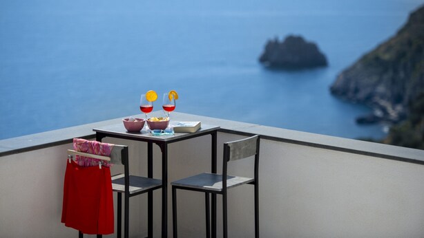 Un balcon avec une table dressée pour deux personnes, offrant une vue sur la côte et un promontoire rocheux au loin.