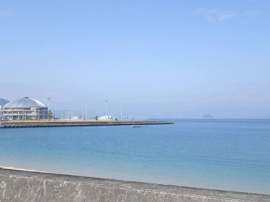 A coastal view with a clear sky, a body of water, a distant island, and a modern building with a dome structure.