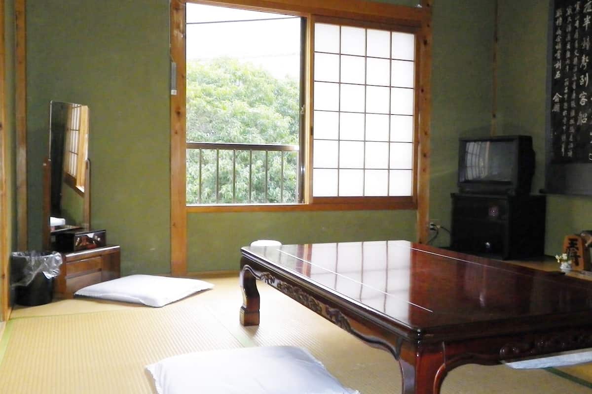 A traditional Japanese room with tatami flooring, a low wooden table, a television, and a shoji screen.