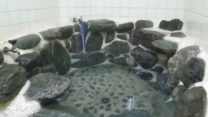 A stone-lined hot tub with a faucet and a stone wall. - Kadota Ryokan (Imabari)