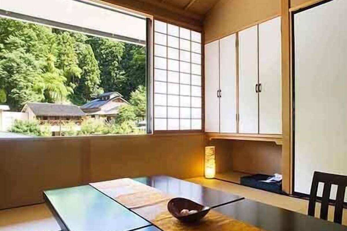 Una habitación japonesa tradicional con suelo de tatami, una mesa baja, puertas correderas y vistas a la vegetación exterior.