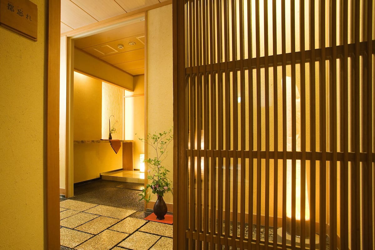 Un pasillo con un tradicional panel japonés shoji, piso de baldosas y una planta en maceta.