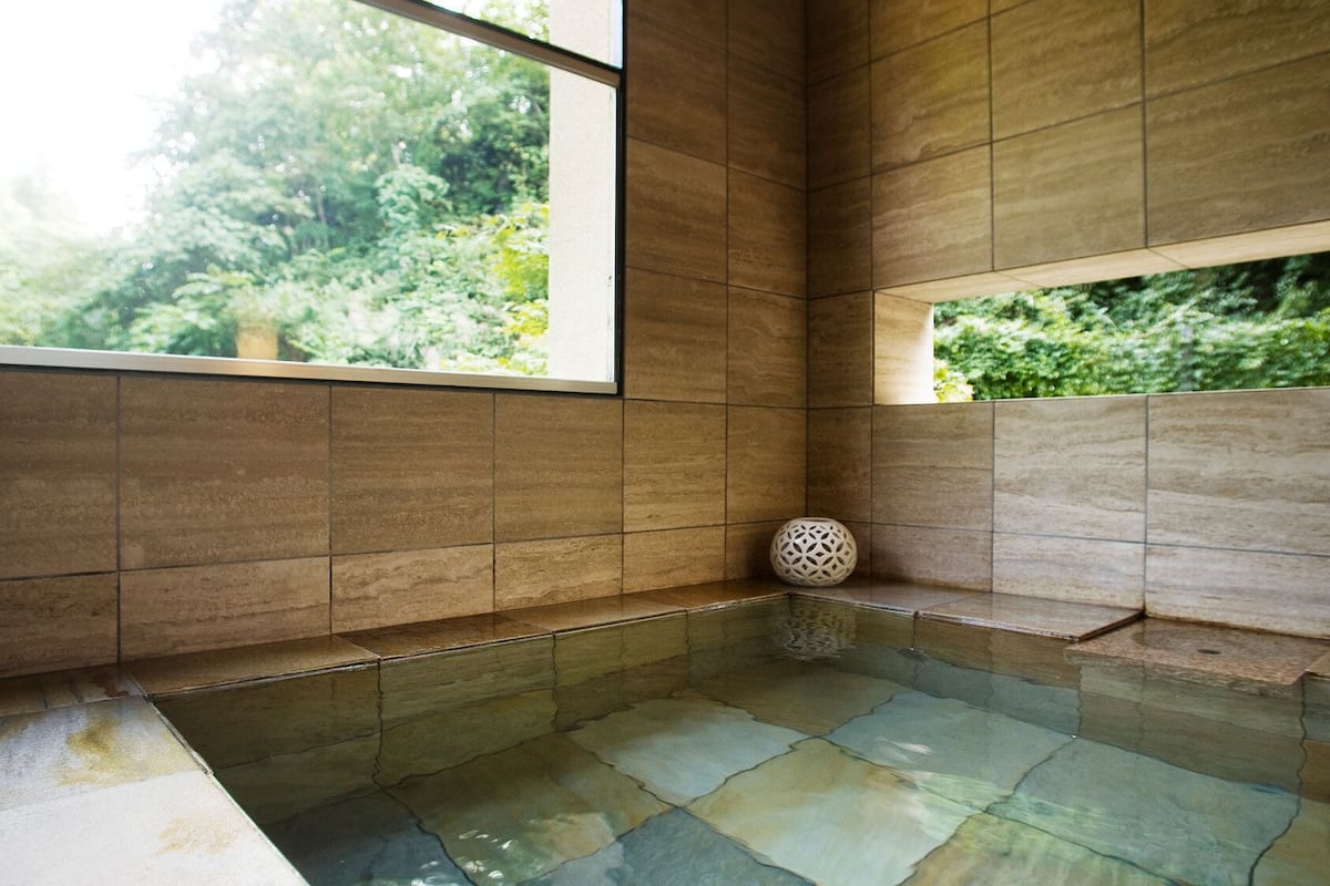 Una habitación con suelo de piedra, un banco y una ventana que da a vistas de vegetación.