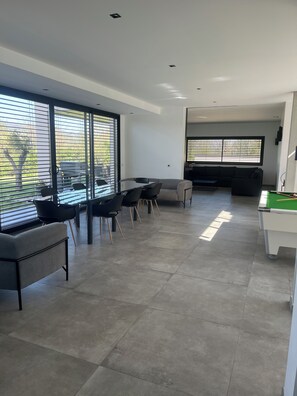 A modern living room with a dining area, large windows, and a pool table.