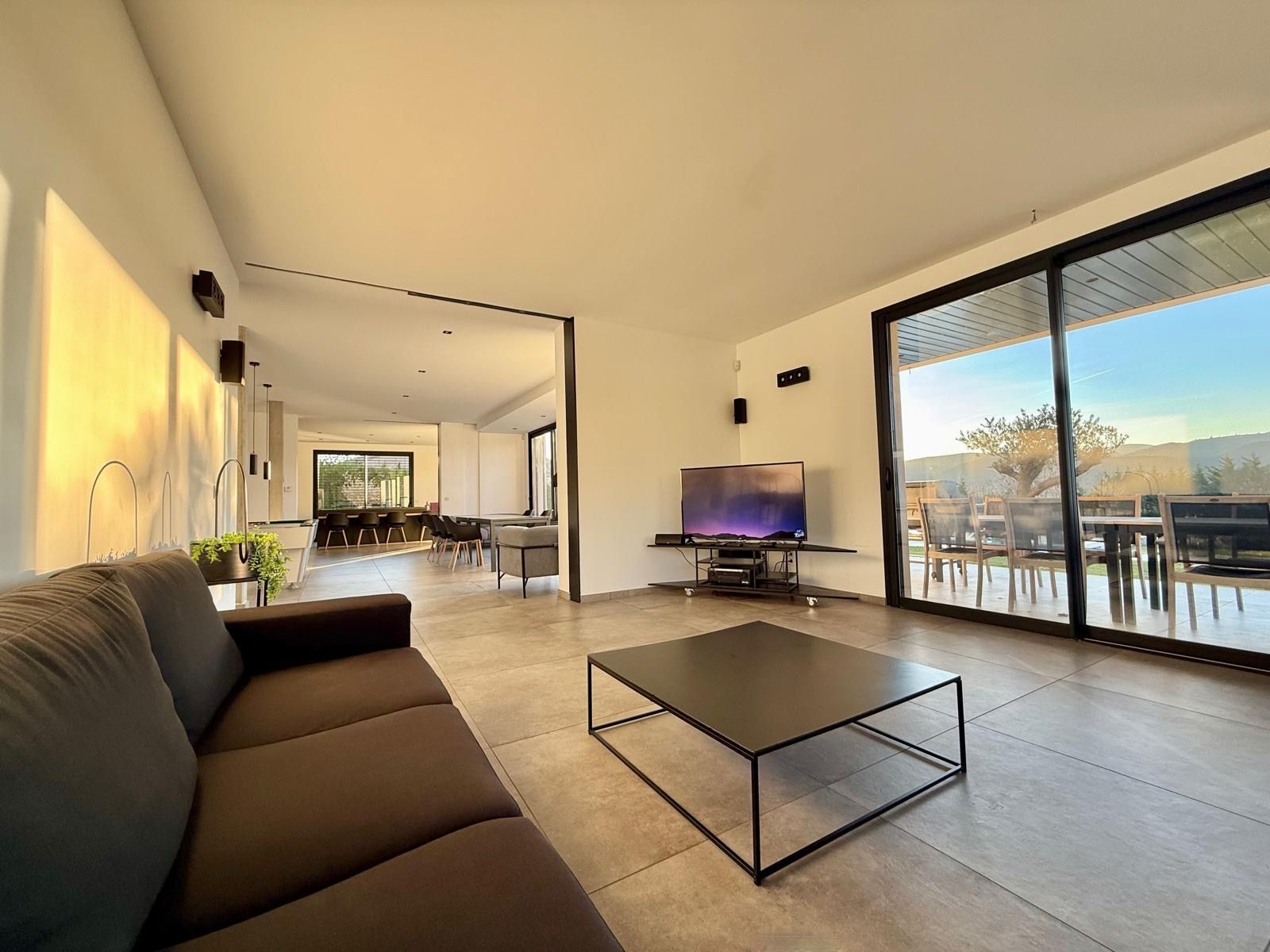 Un salon moderne avec un canapé, une table basse et un téléviseur. On aperçoit à l’arrière-plan un coin repas avec des chaises et une table.