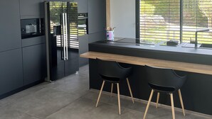 A modern kitchen with dark cabinetry, a wooden countertop, and two black bar stools. - VILLA_DE_VACANCES_LA_PINATTE (Saint-Péray)