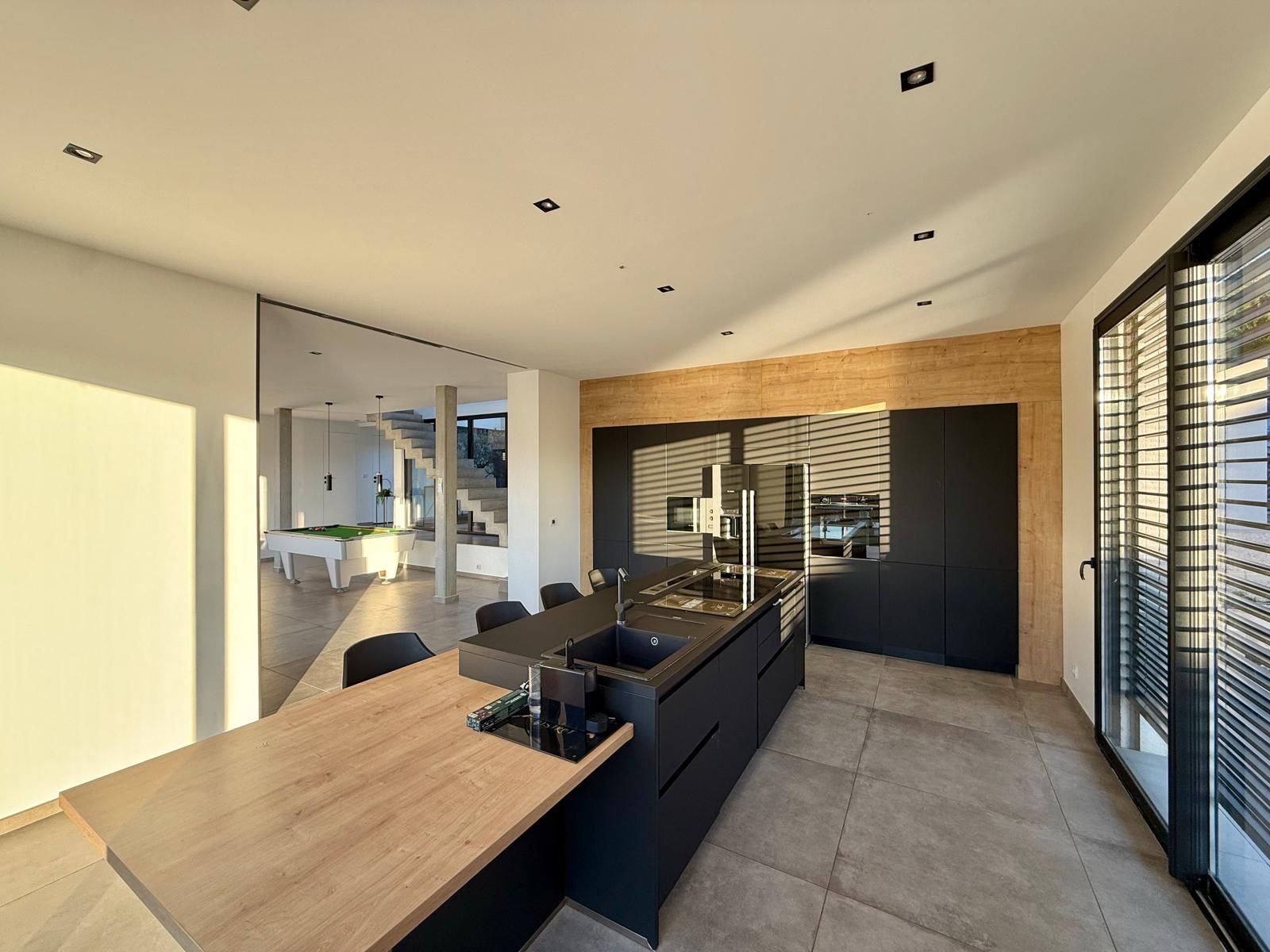 A modern kitchen with a wooden countertop, black cabinetry, and a built-in island.