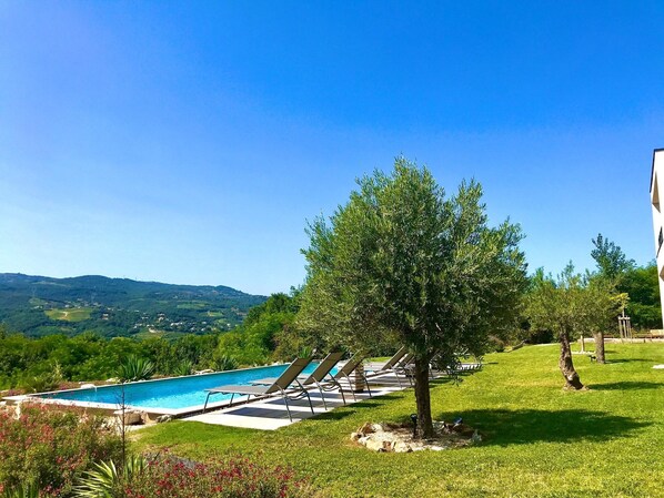 A swimming pool with lounge chairs, a tree, and a view of hills in the background.