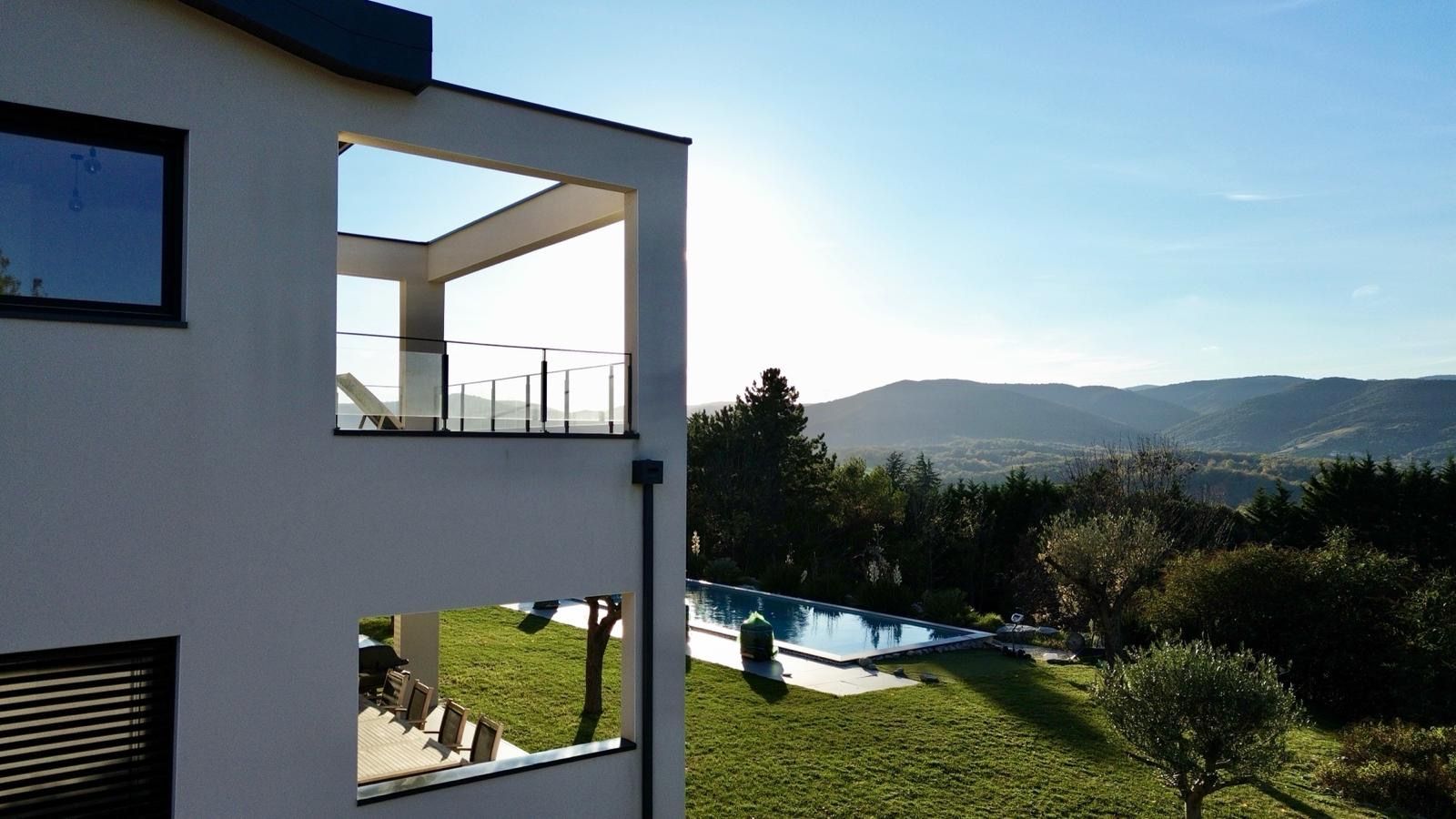 A modern two-story building with a balcony overlooking a swimming pool and a mountainous landscape.