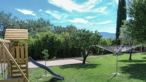 A playground with a slide and climbing structure, surrounded by grass and trees.