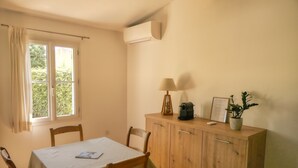 A dining area with a table, chairs, a cabinet with a lamp, a potted plant, and an air conditioning unit.