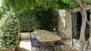 A patio with a round table and chairs, surrounded by lush greenery and a stone wall.