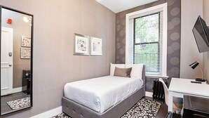 Ein Schlafzimmer mit einem Bett, einem Schreibtisch, einem Stuhl, einem Spiegel und einem Fenster mit Jalousien.